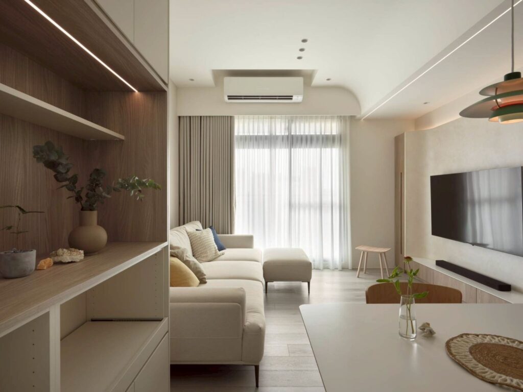 沐馨窗簾　搭配客廳大面積落地窗與米白沙發、木質收納牆面，選用低彩度米色蛇型布簾，營造一致的沉穩風格，柔紗簾則提升白天採光時的層次感